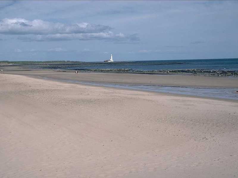 View along sandy shore with lighthouse in background.